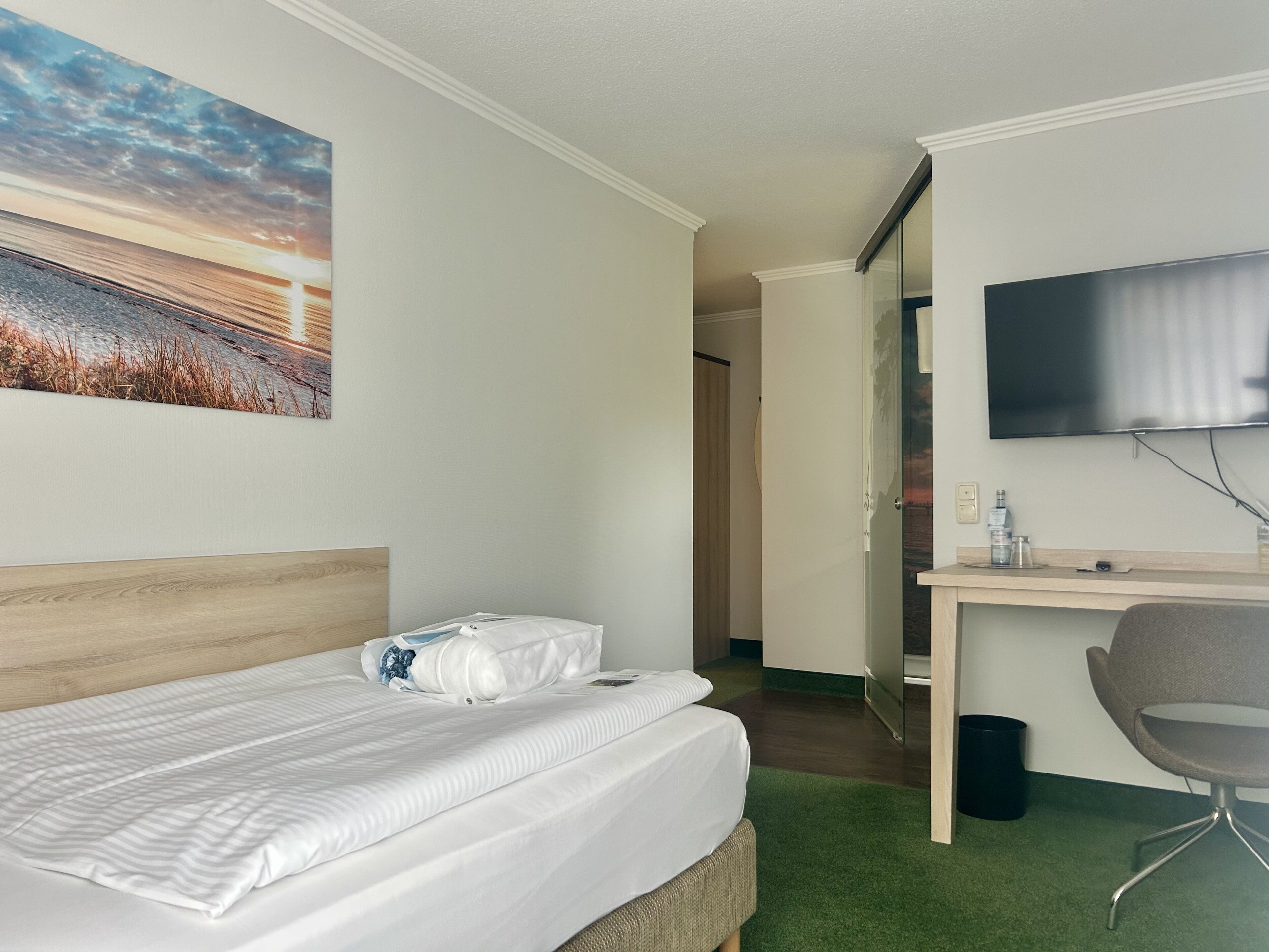 A hotel room with a bed, a desk with a chair, a television, and a painting on the wall.