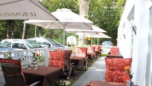 An outdoor dining area with tables and chairs, umbrellas, and a row of parked cars. - Best Western Plus Ostseehotel Waldschloesschen (Ostseebad Prerow)