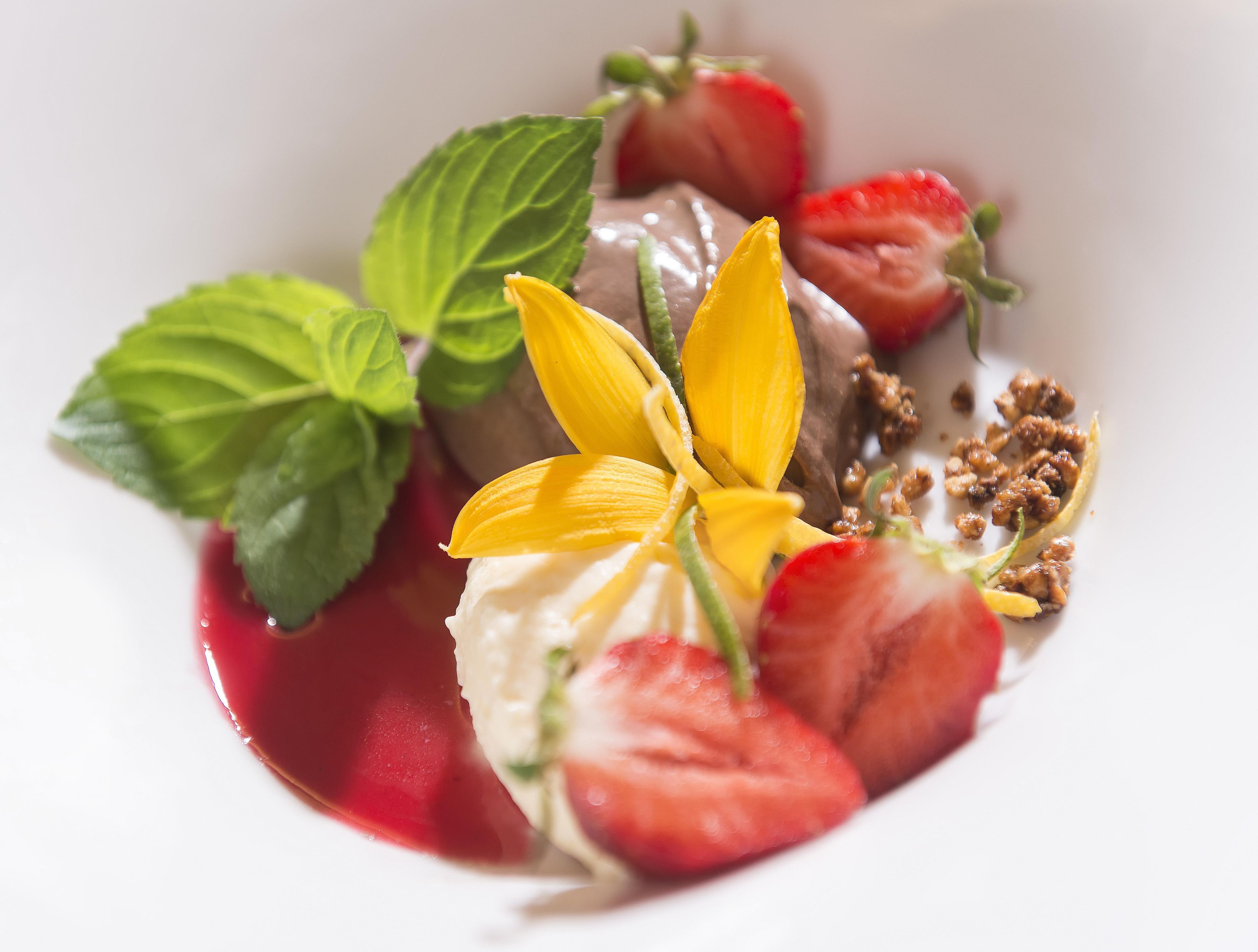 Un postre con fresas, hojas de menta y una flor amarilla sobre un plato blanco.