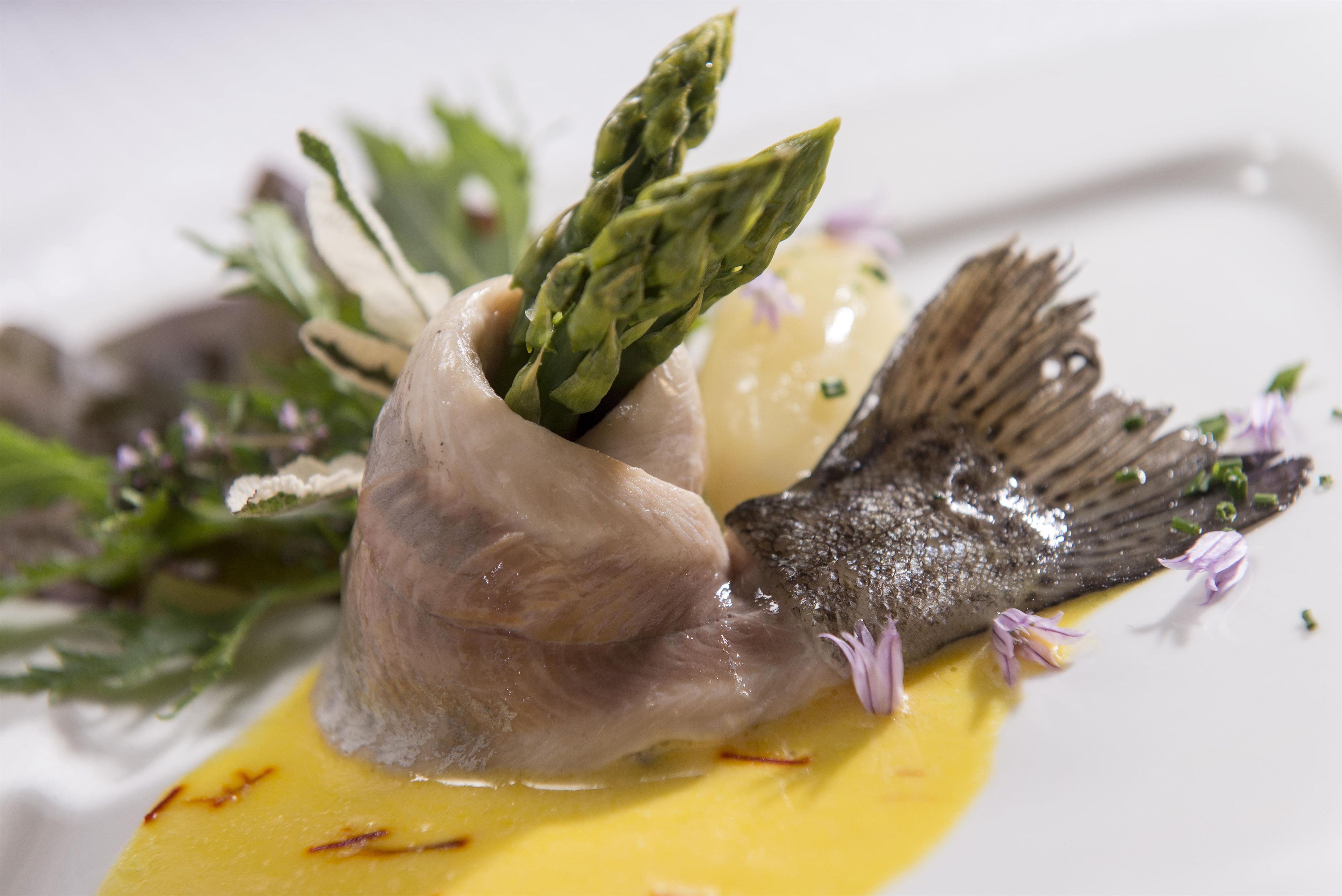 Un piatto con del pesce, asparagi e una salsa gialla.
