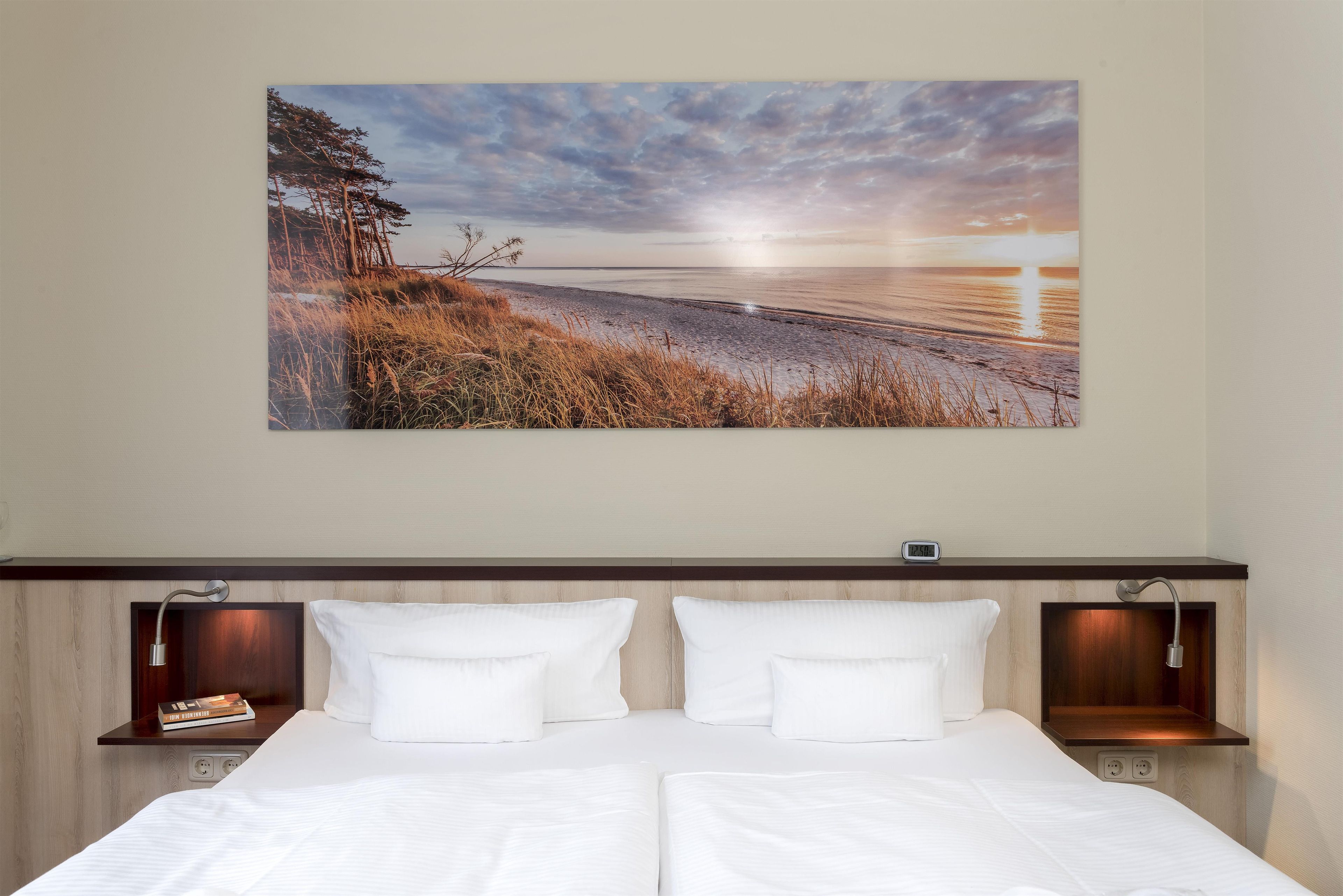 A bedroom with a bed, two bedside tables, and a wall-mounted artwork depicting a beach scene.
