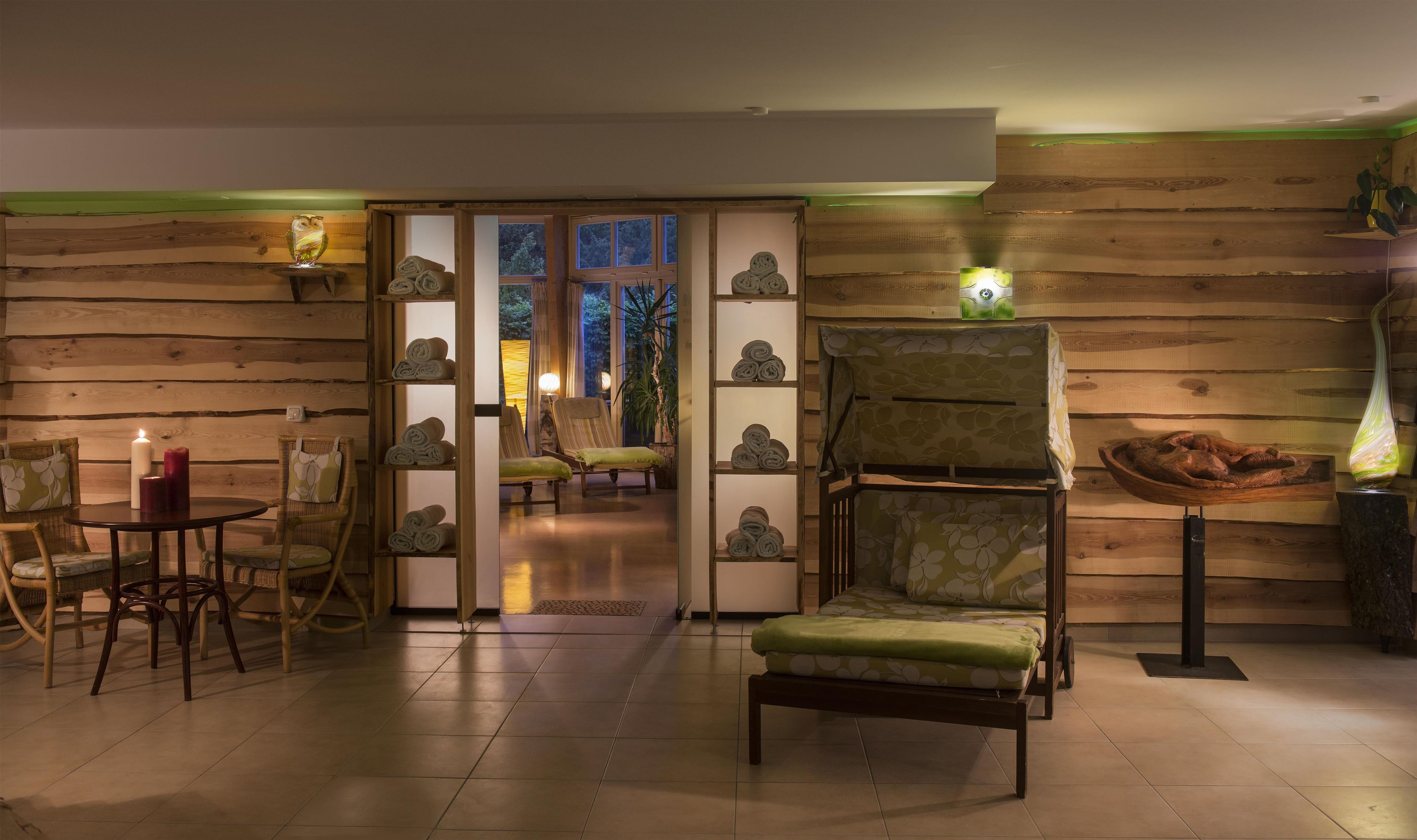A room with a wooden wall, a chair, a table with candles, and a view through a glass door.