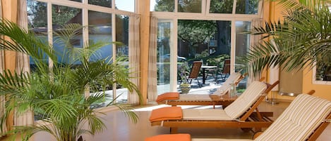 Una habitación luminosa con grandes ventanales, una mesa de billar, sillones de descanso y una planta en maceta.