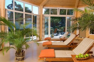 Una habitación luminosa con grandes ventanales, una mesa de billar, sillones de descanso y una planta en maceta.