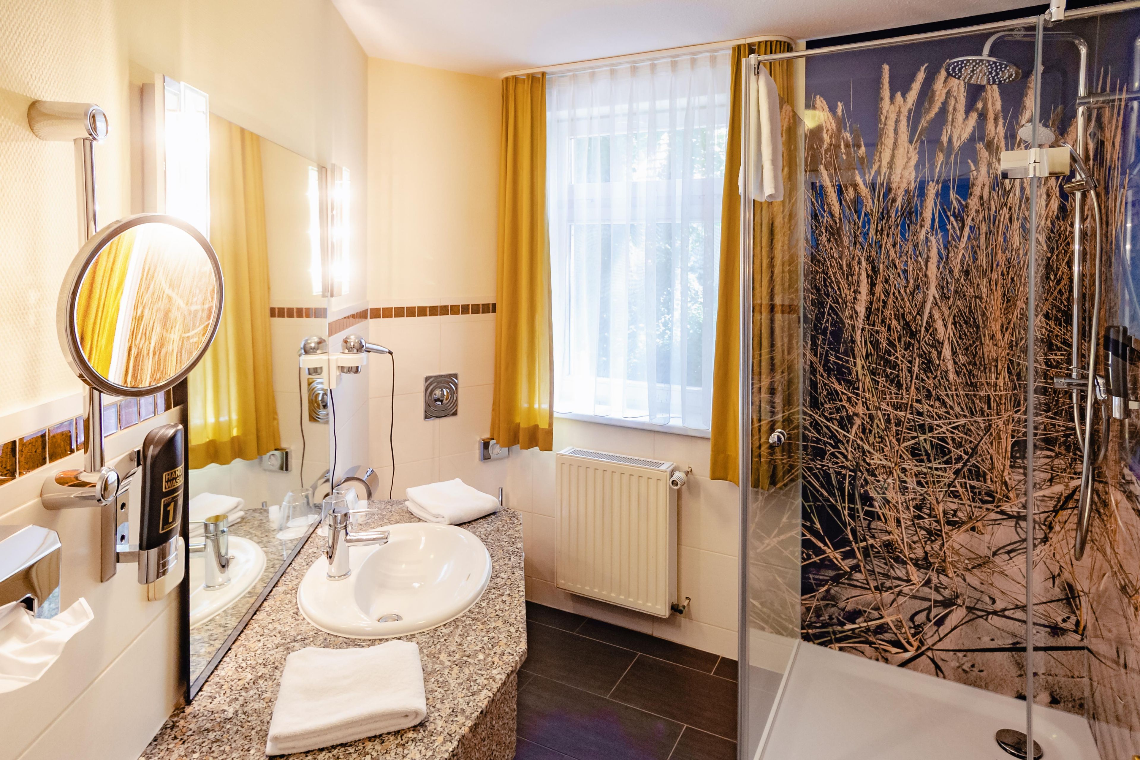 A modern bathroom with a granite countertop, a white sink, a handheld showerhead, and a glass shower enclosure with a decorative wall.