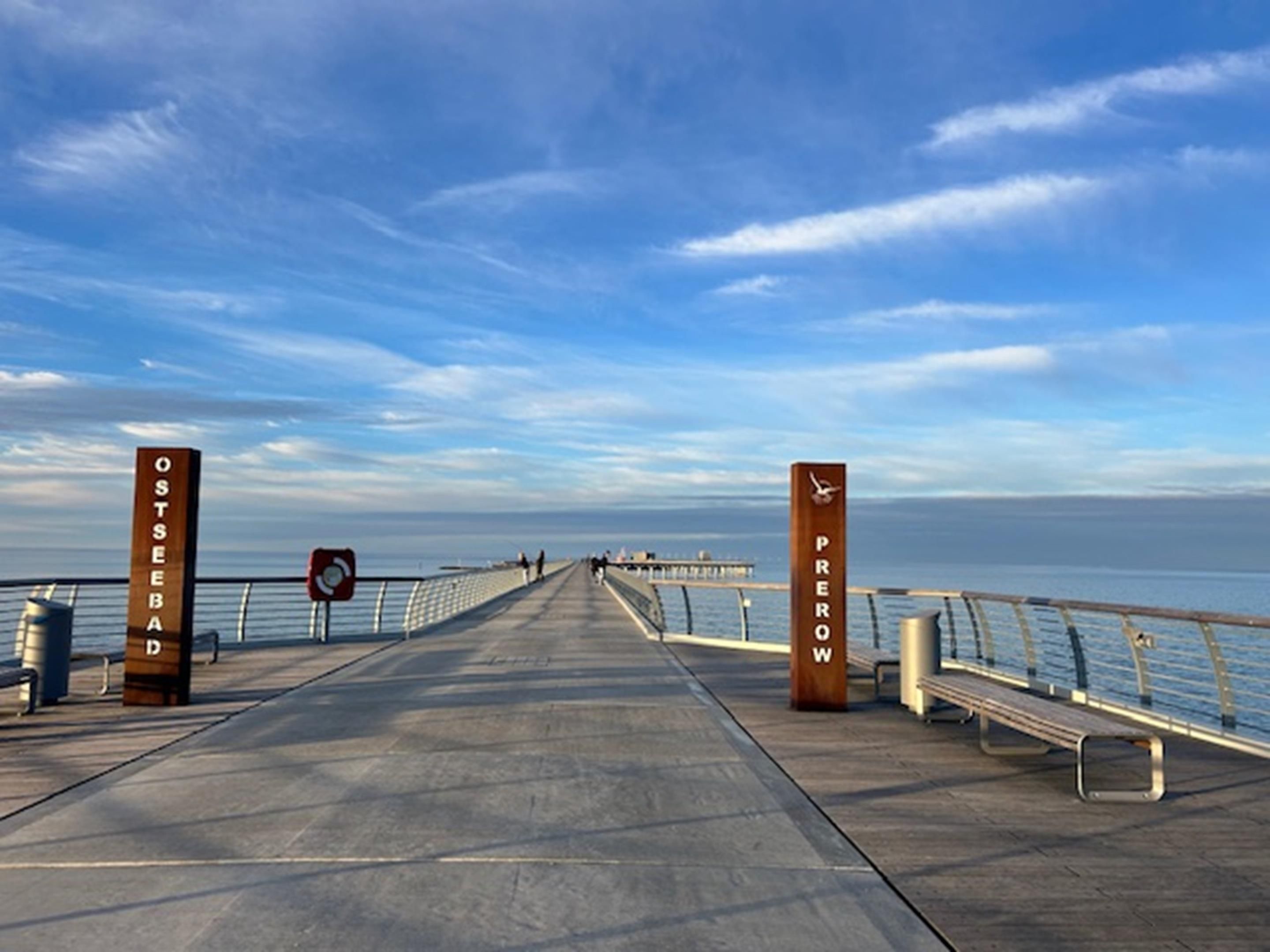 Une jetée s’avançant dans l’eau, agrémentée de bancs et de garde-corps, et sur laquelle on peut lire deux panneaux indiquant « OSTSEBA » et « PEREW ».