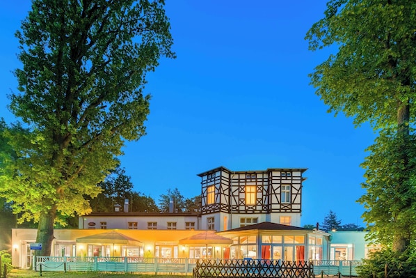 Een klassiek Europees gebouw met een opvallende toren, een overdekt terras en een verzorgde tuin.