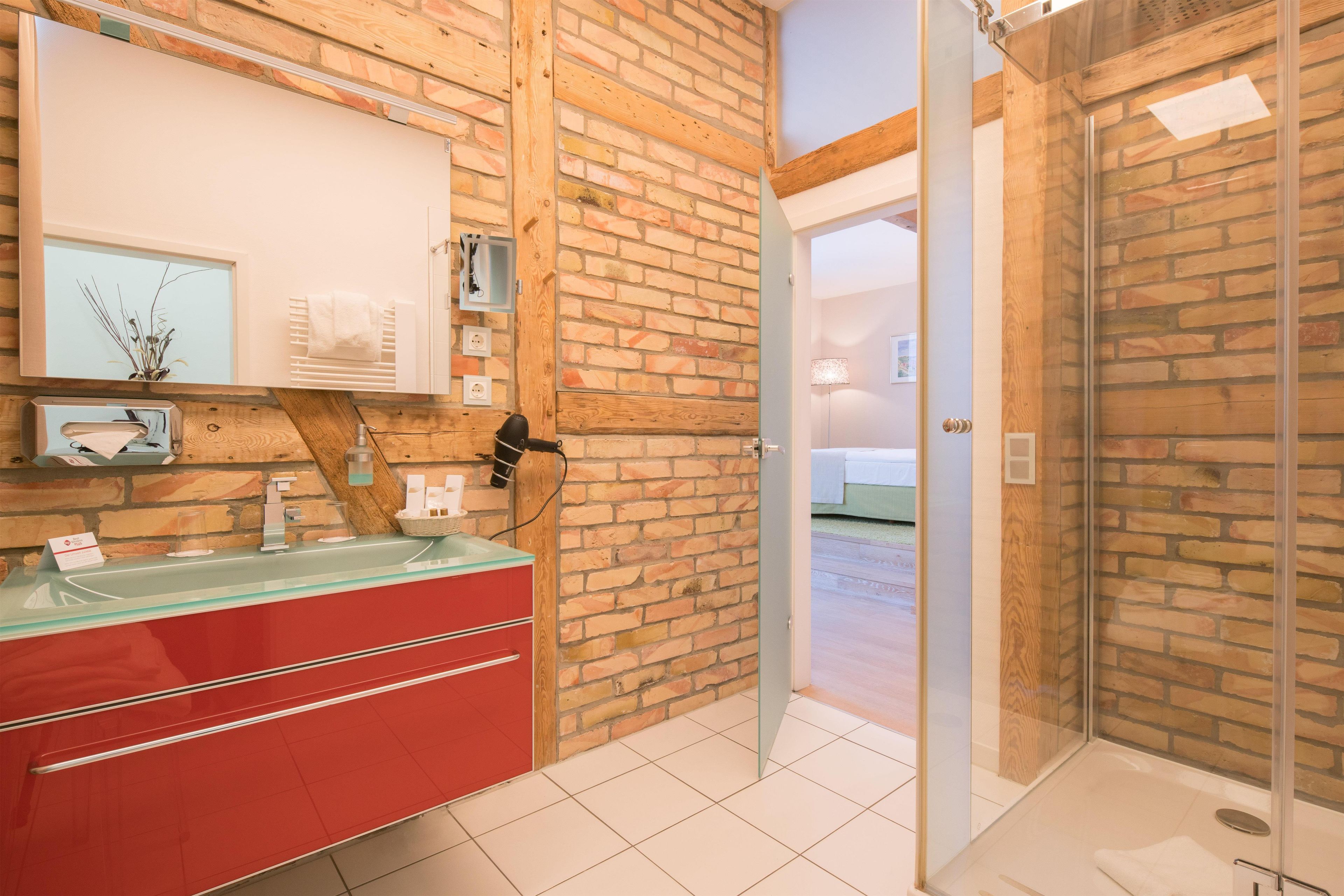 Un baño con tocador rojo, cabina de ducha con mampara de vidrio y pared de ladrillo.