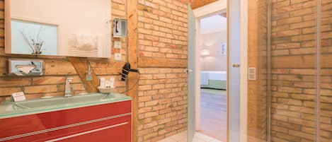 Casa de banho com toucador vermelho, cabine de chuveiro em vidro e parede de tijolo.