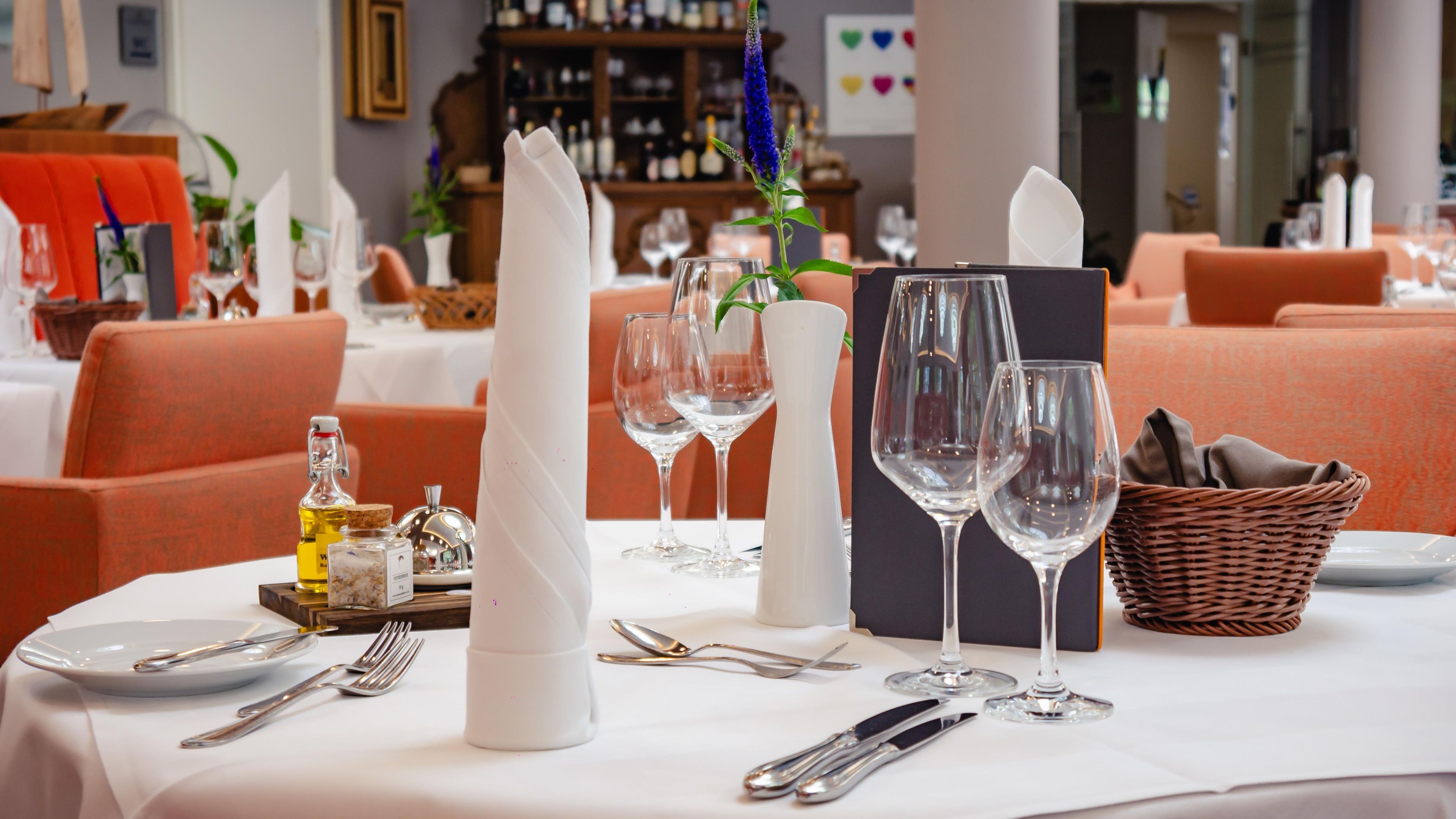 A dining table set with wine glasses, cutlery, and a vase with a blue flower.
