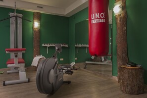 Een sportschool met groene wanden, houten vloeren en fitnessapparatuur, waaronder een rode bokszak met de tekst 'U.N.O. SPORTS'.