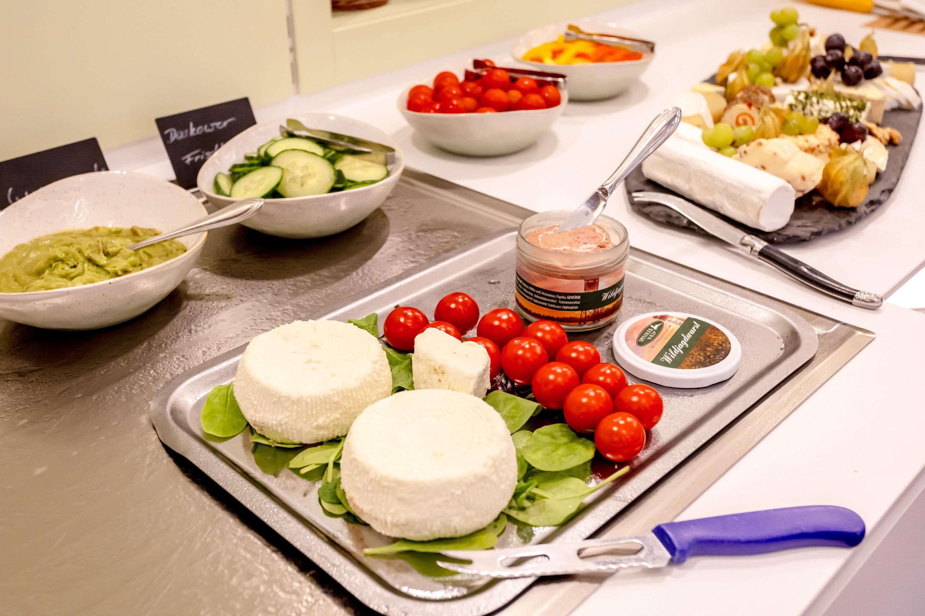 Een buffet met diverse etenswaren, waaronder kaas, tomaten en een smeersel.