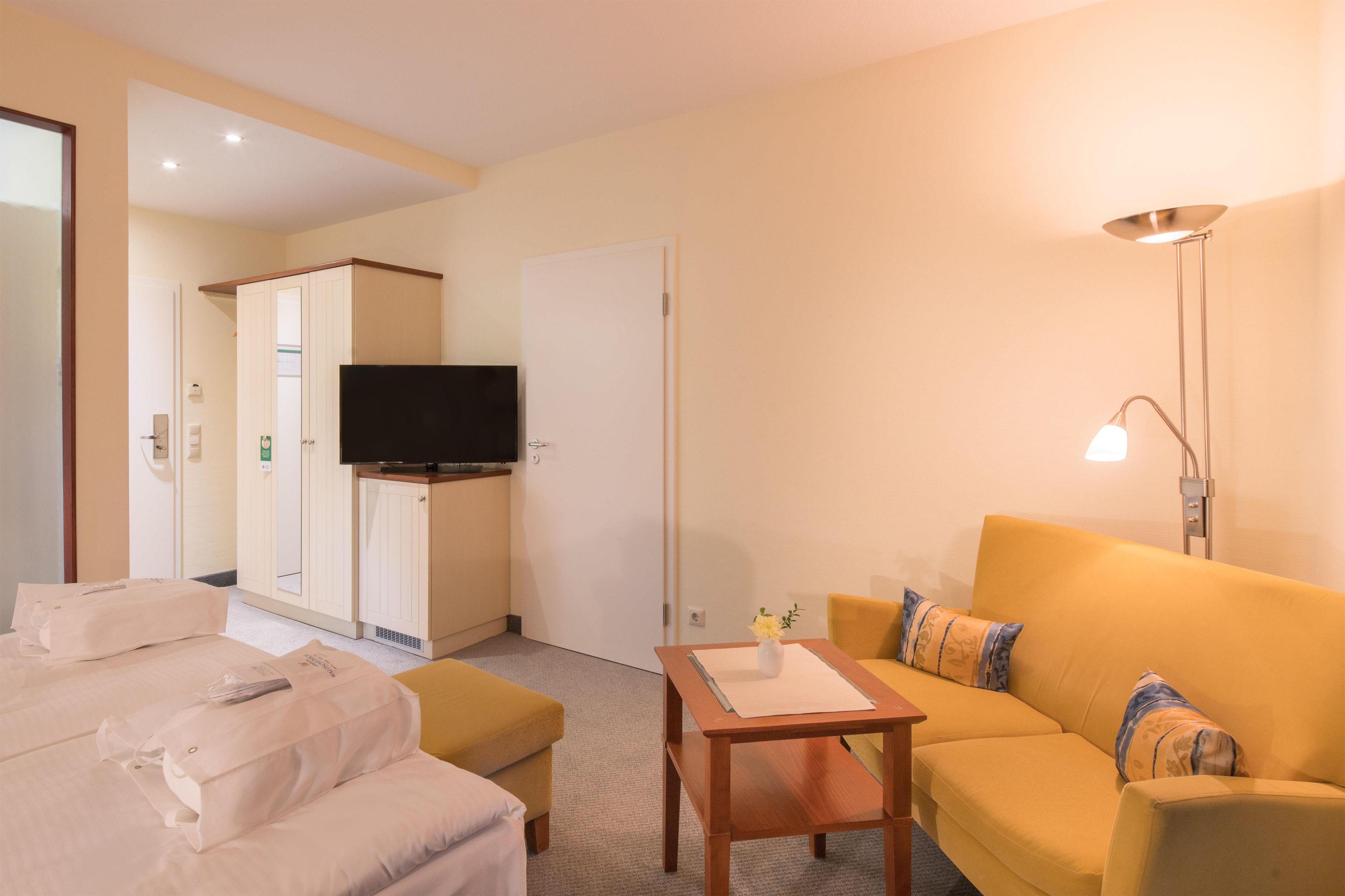A hotel room with a sofa, a small table, a television, and a wardrobe.