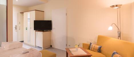A hotel room with a sofa, a small table, a television, and a wardrobe.