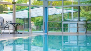 Une piscine intérieure avec des parois en verre transparent, un espace détente avec des fauteuils et une vue sur la verdure environnante.