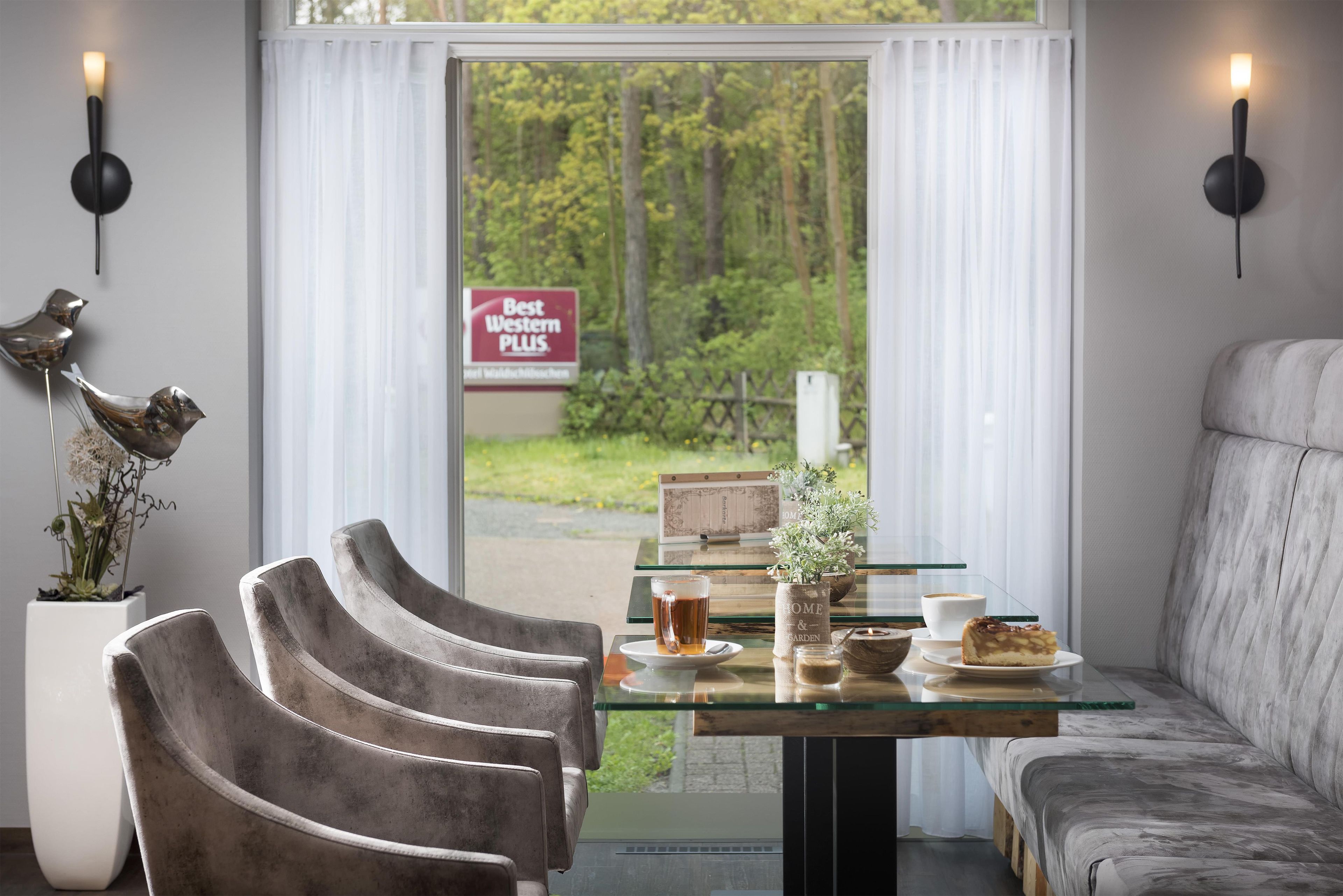 A modern interior with a sofa, chairs, a glass table, and a view of a forest through a window.
