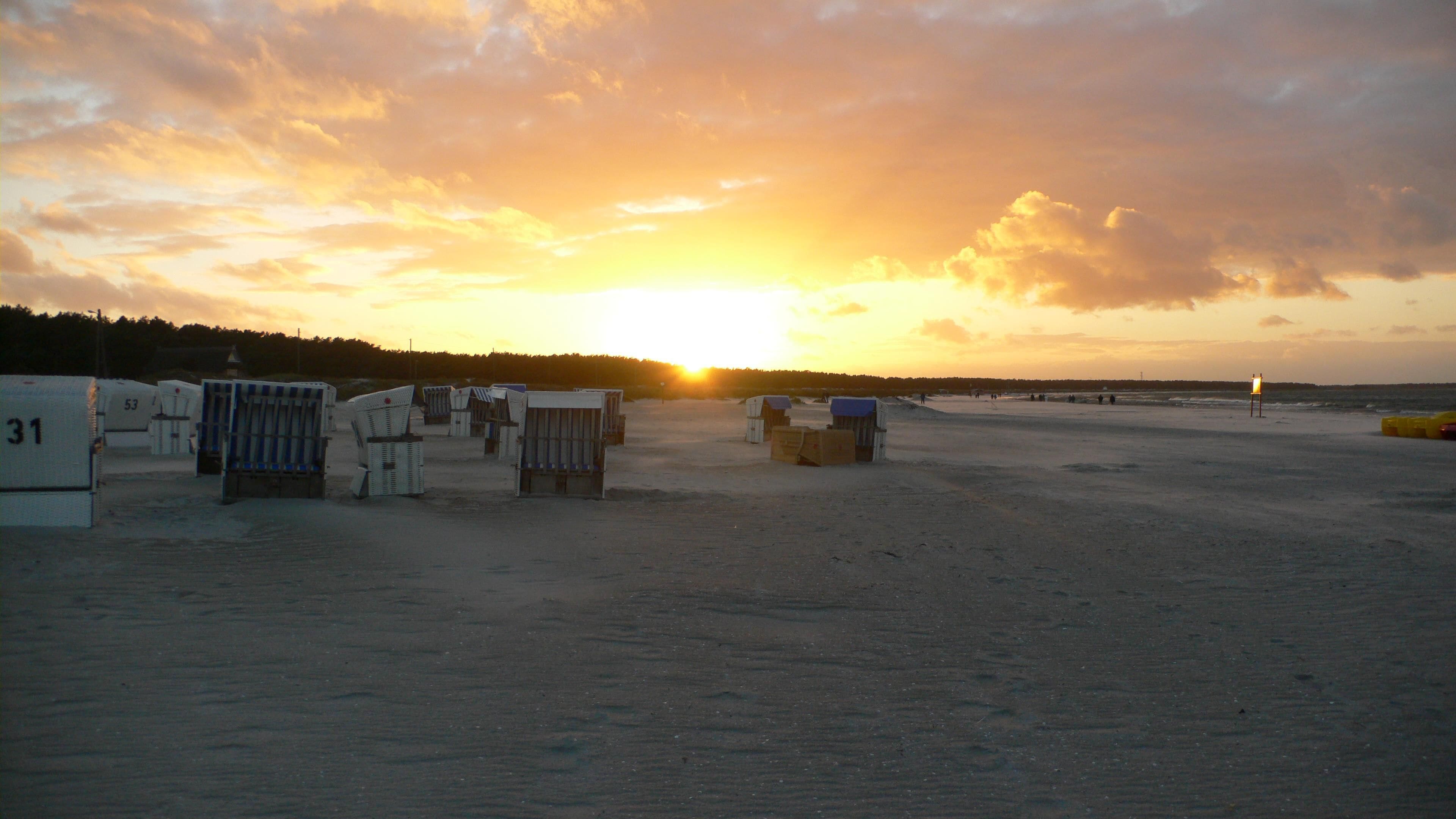 A beach with beach chairs and a sign, under a sunset sky.