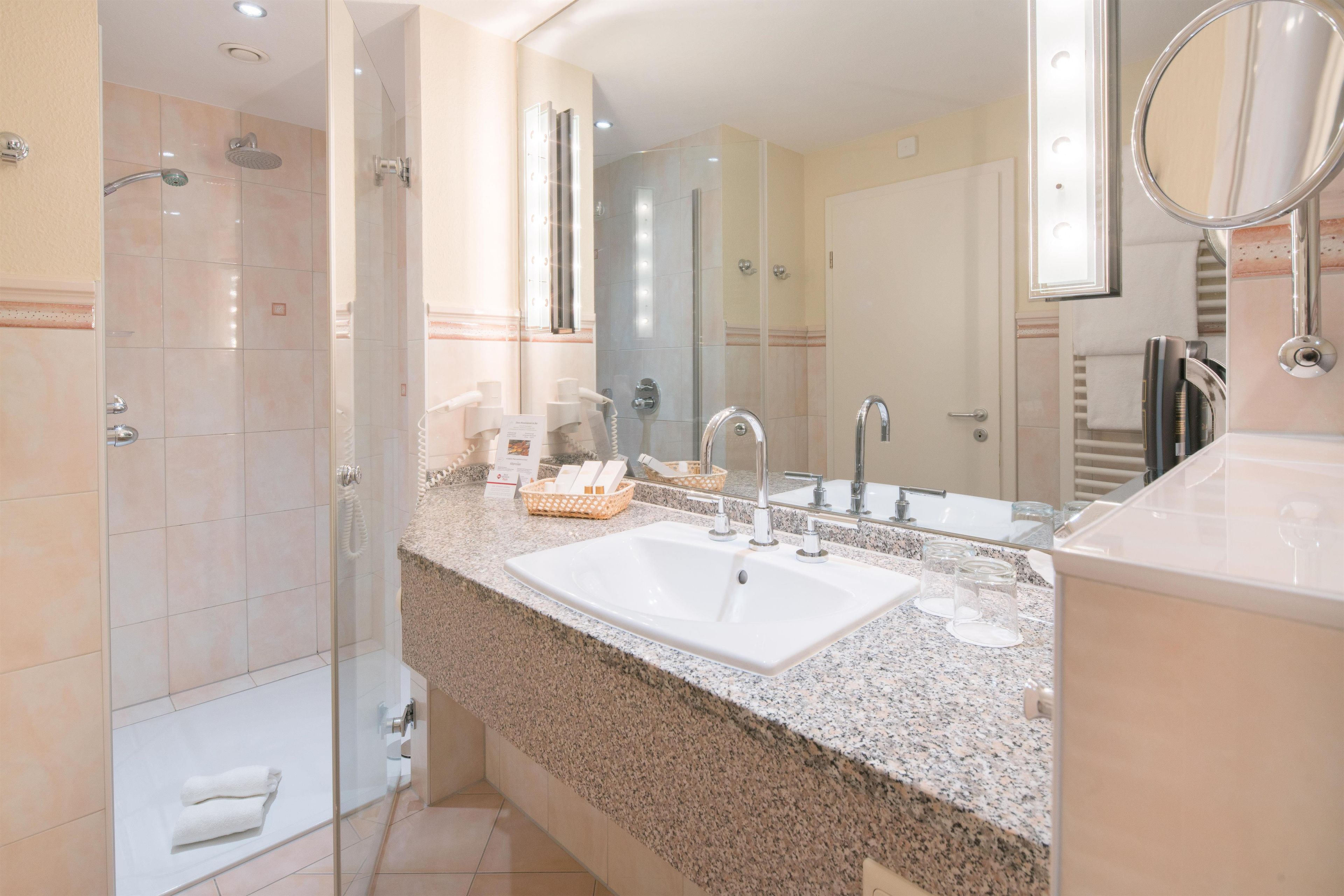 A modern bathroom with a large sink, a glass shower enclosure, and a vanity with a mirror.