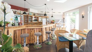 A bar area with wooden stools, a glass table, wicker chairs, and a variety of bottles on shelves. - Best Western Plus Ostseehotel Waldschloesschen (Ostseebad Prerow)