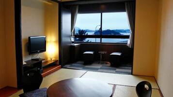 A hotel room with a television, a round table, two chairs, a sofa, and a view of a body of water.