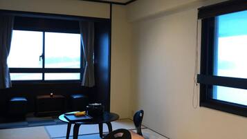 A room with tatami mats, a low table with a chair, a sofa, and a large window with curtains.