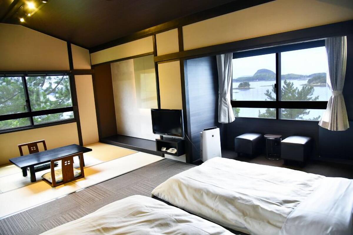 A hotel room with a bed, a TV, a small table, and a view of the water.