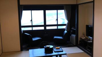 A room with a large window, two chairs, a table, a TV, and a small kitchenette.