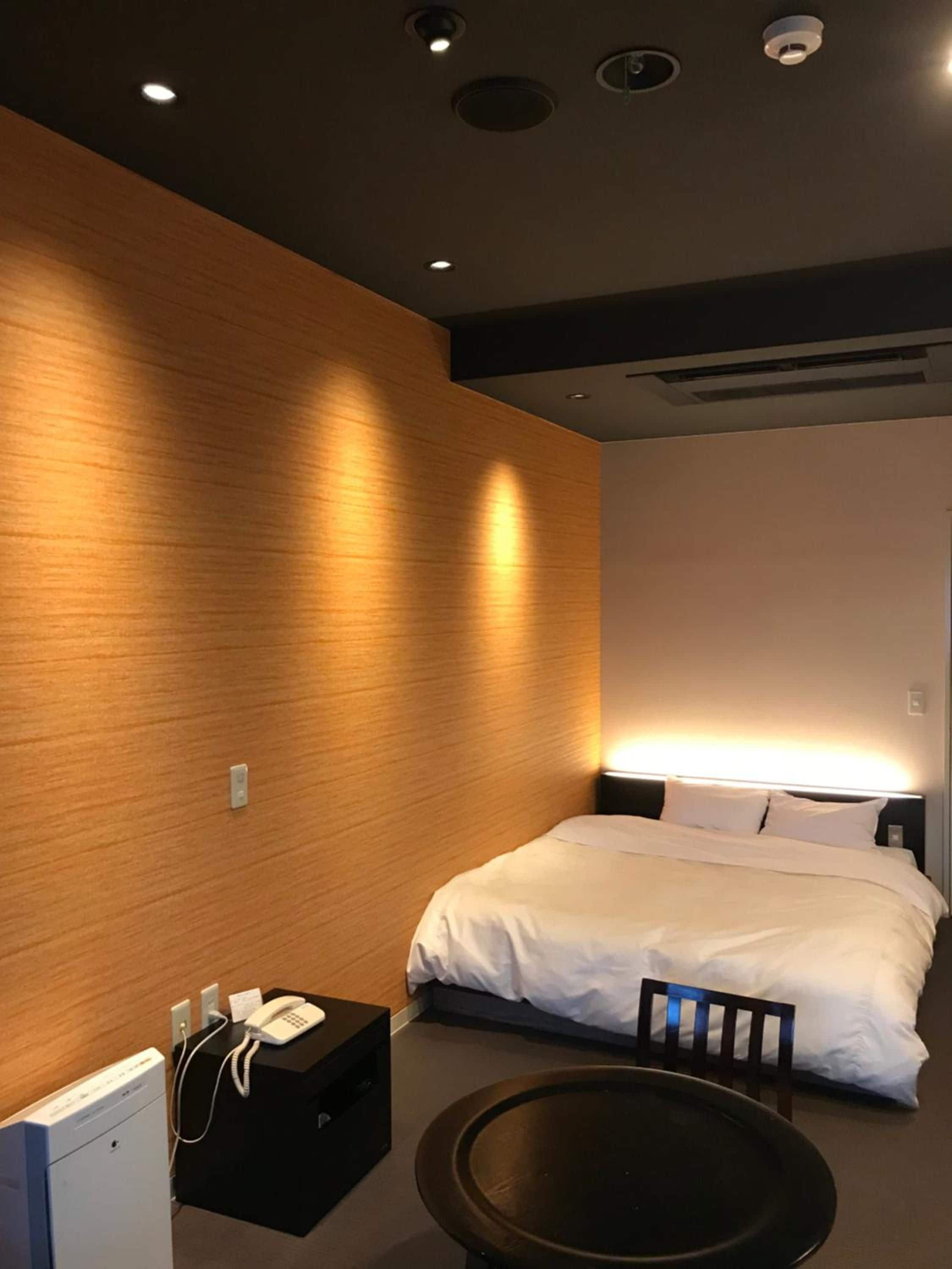 A hotel room with a bed, bedside table, and a desk with a phone.