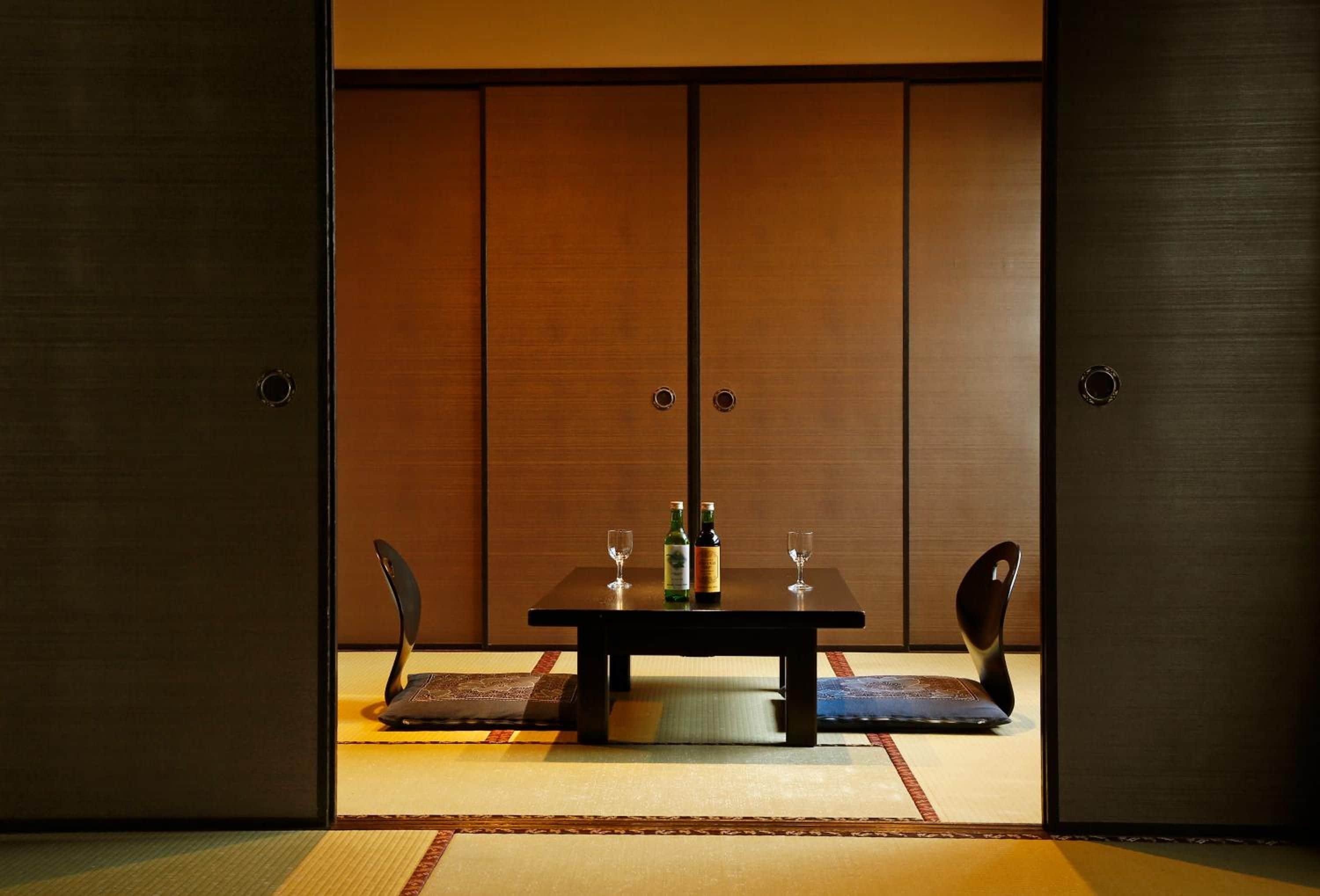 A traditional Japanese room with tatami flooring, a low table with two chairs, and a sliding door with a wooden finish.