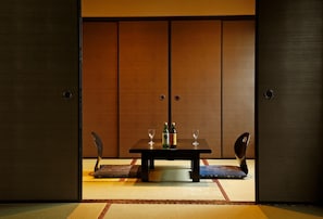 Ein traditioneller japanischer Raum mit Tatami-Bodenbelag, einem niedrigen Tisch mit zwei Stühlen und einer Schiebetür aus Holz.