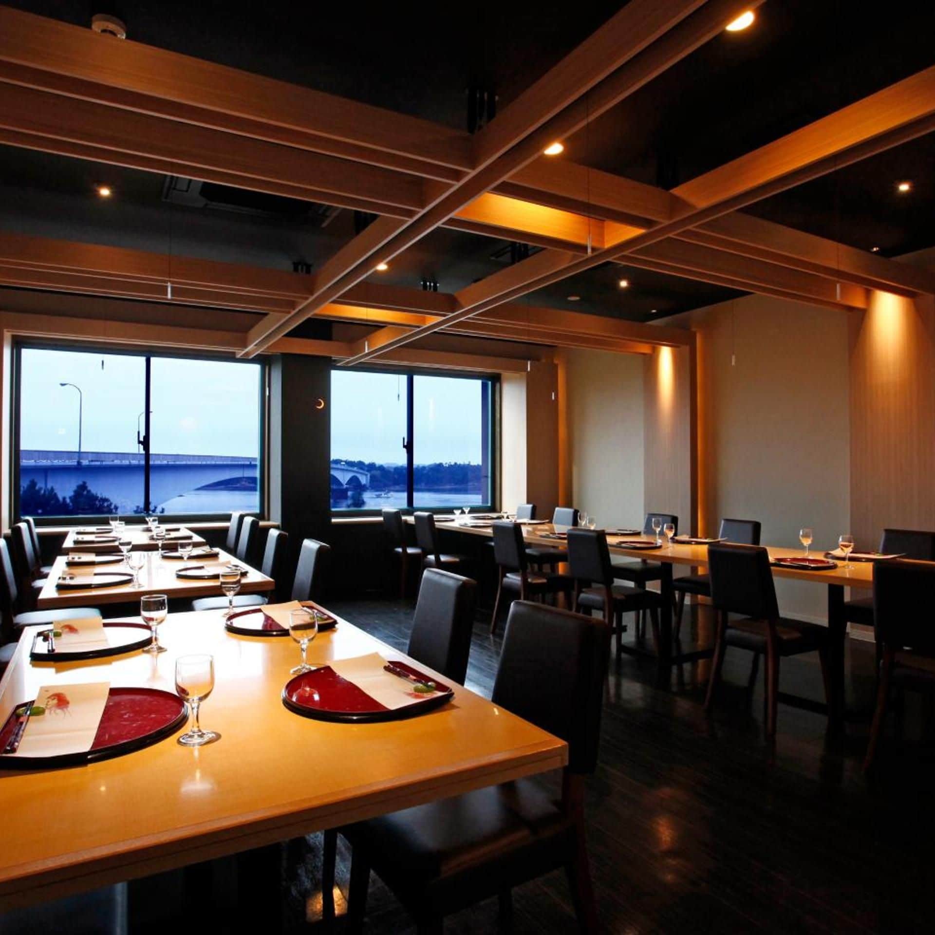 Un salón de conferencias con mesas dispuestas para comer, ventanas amplias con vista a un puente y un diseño de techo moderno.