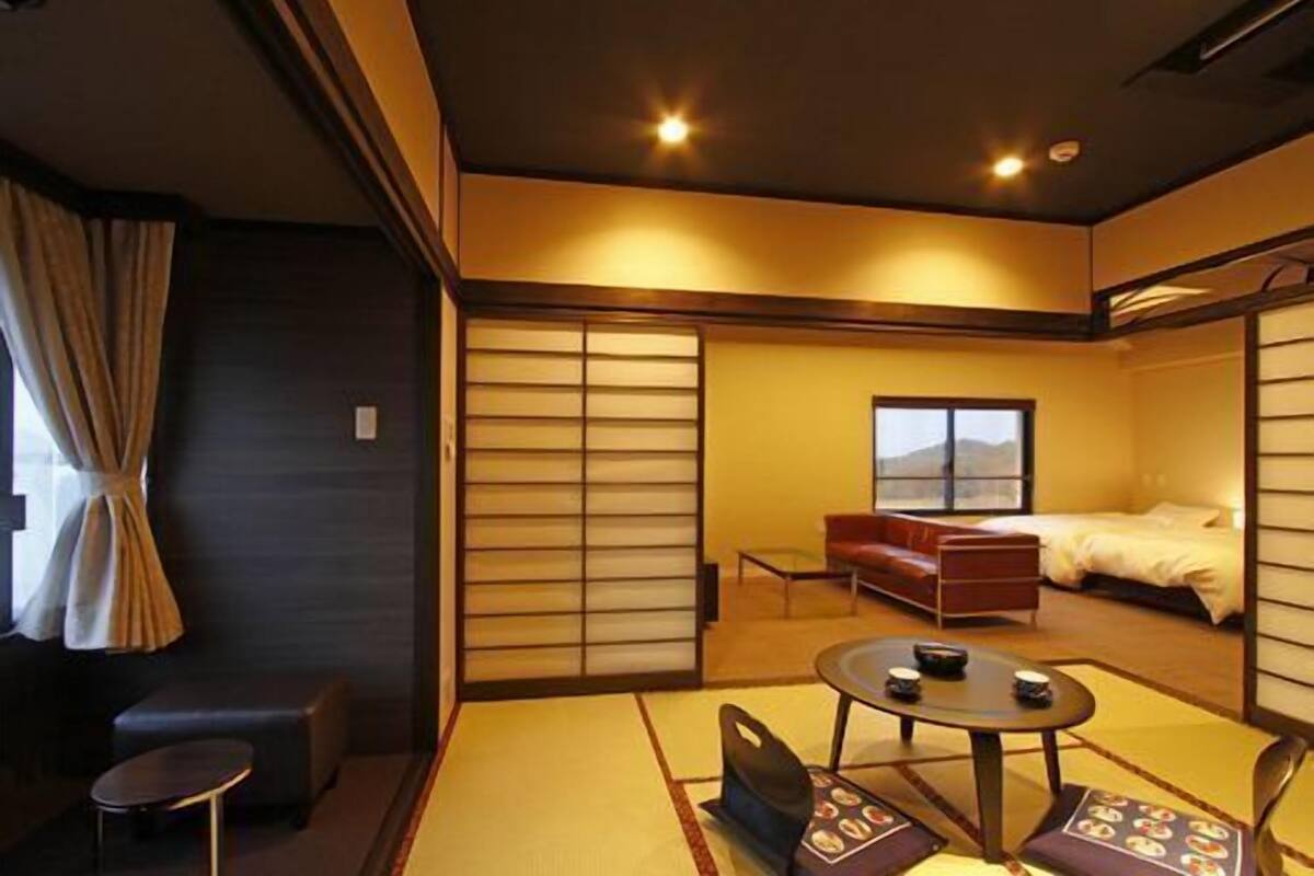 A traditional Japanese-style room with tatami flooring, a low table with cups, a sofa, and a bed with a view.