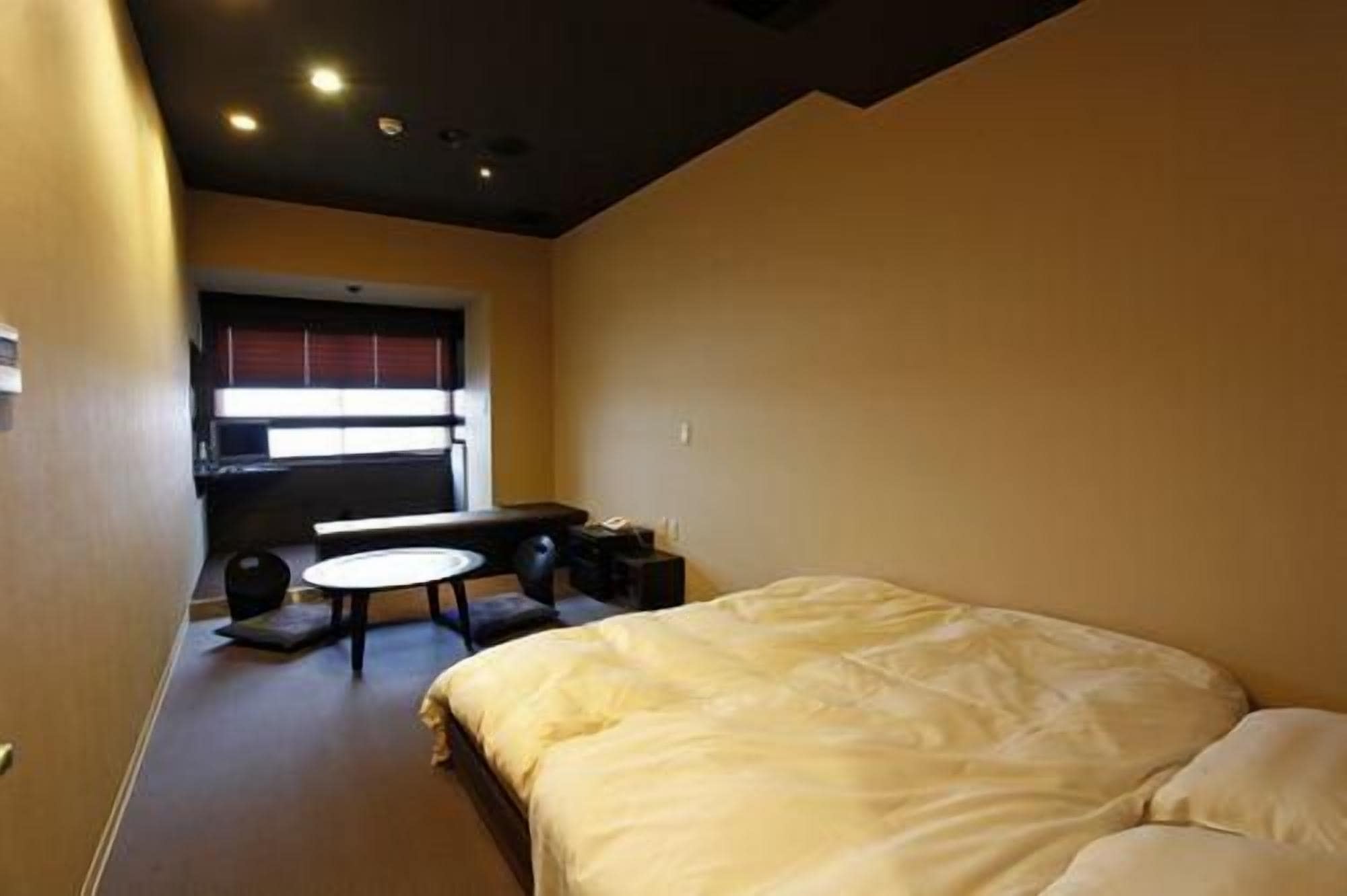 A hotel room with a bed, a small table, and a window with blinds.