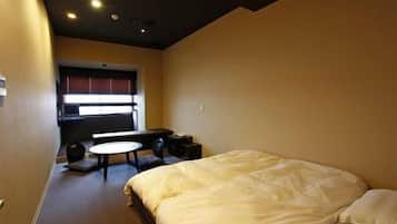 A hotel room with a bed, a small table, and a window with blinds.