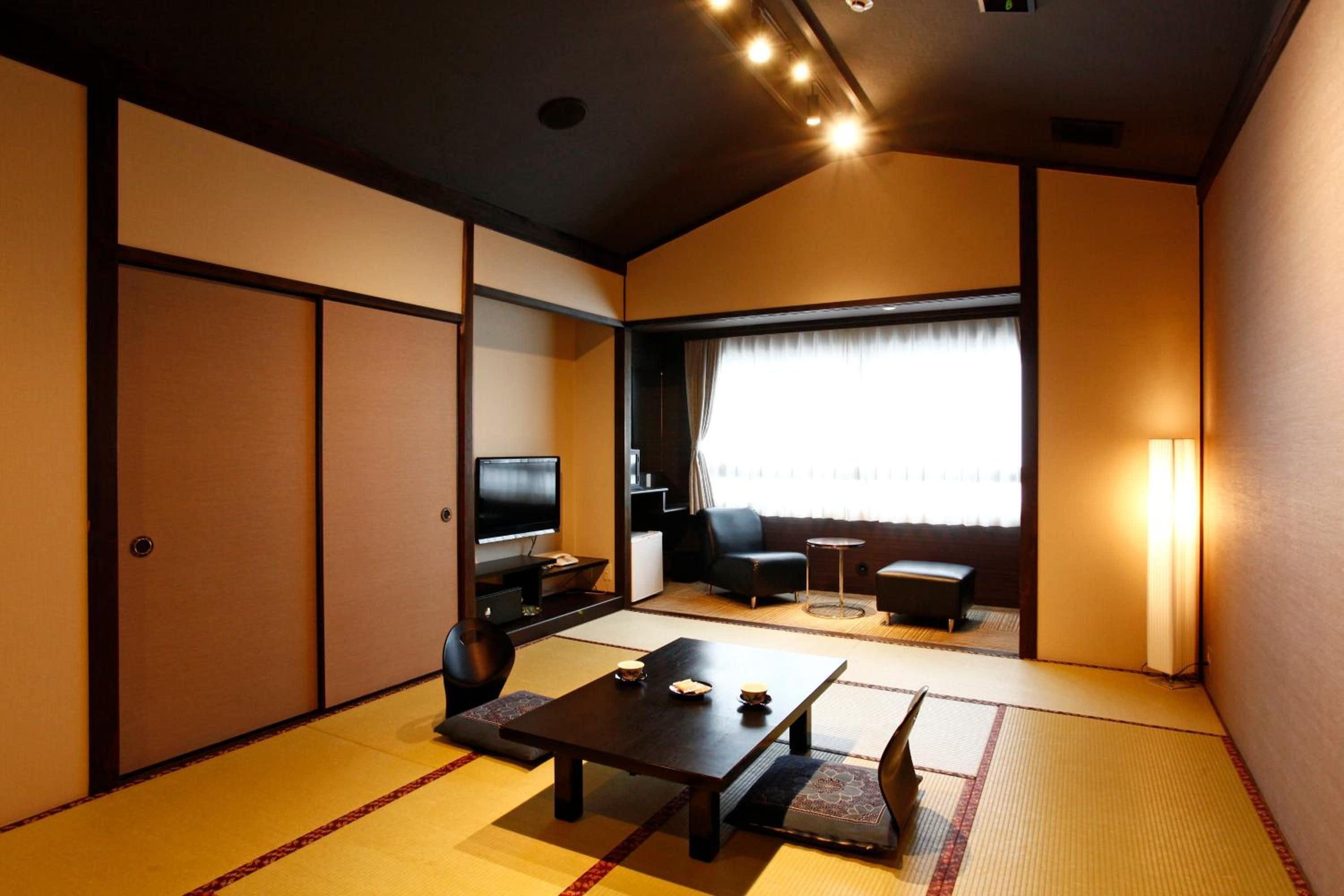 A traditional Japanese-style room with tatami flooring, a low table, a sofa, and a television.