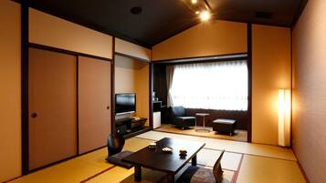 A traditional Japanese-style room with tatami flooring, a low table, a sofa, and a television.