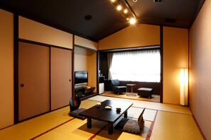 A traditional Japanese-style room with tatami flooring, a low table, a sofa, and a television. - Hotel Shosenkaku Romankan (Kamiamakusa)