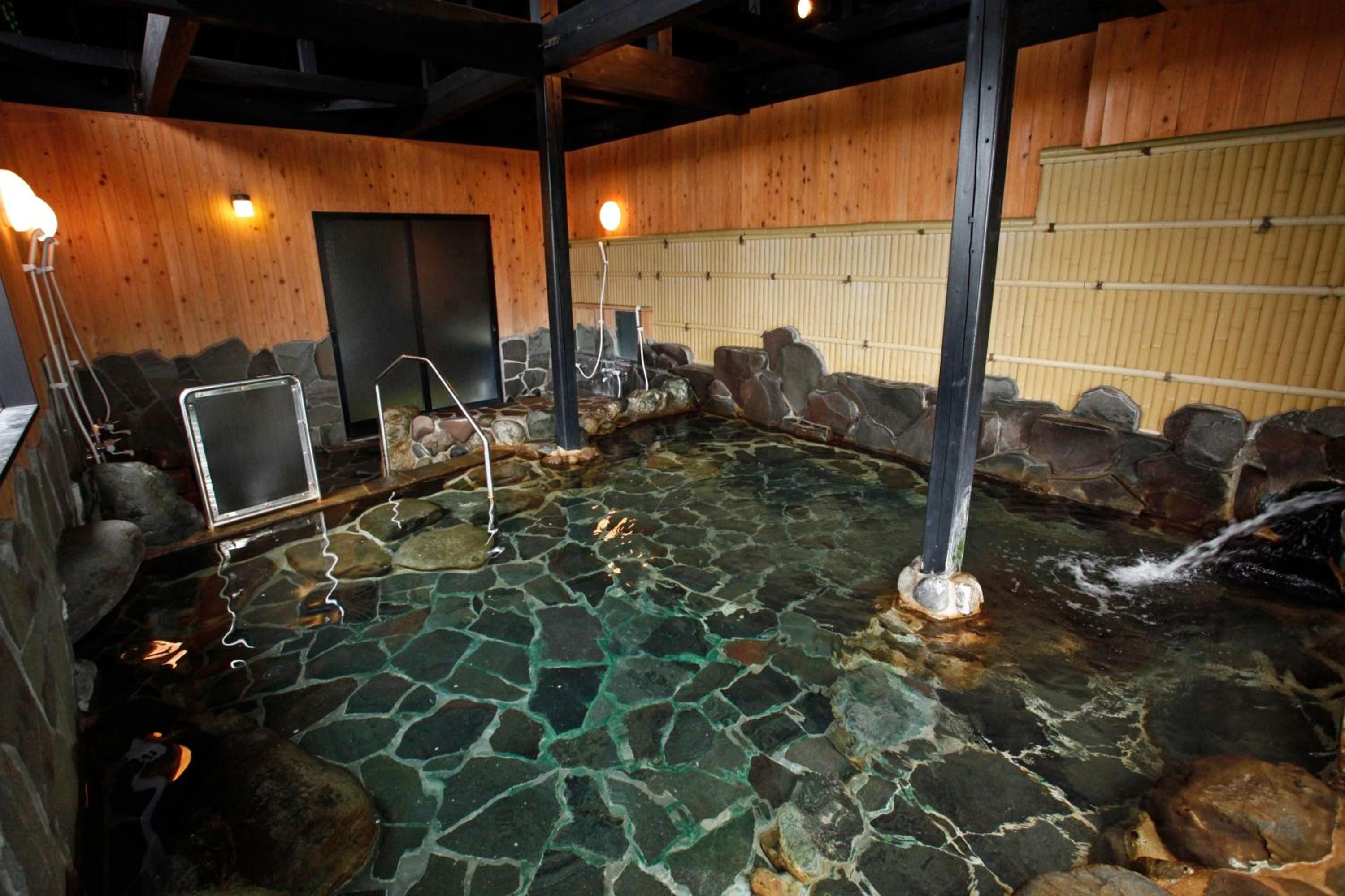 Un jacuzzi de piedra con agua cristalina, rodeado de paredes de madera y detalles de piedra.