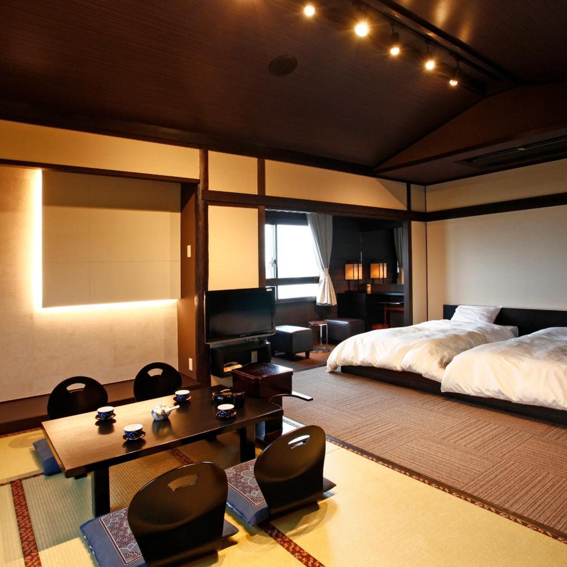 Una habitación de hotel con cama, escritorio con sillas, televisor y ventana con cortinas.