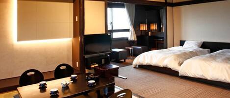 A hotel room with a bed, a desk with chairs, a television, and a window with curtains.