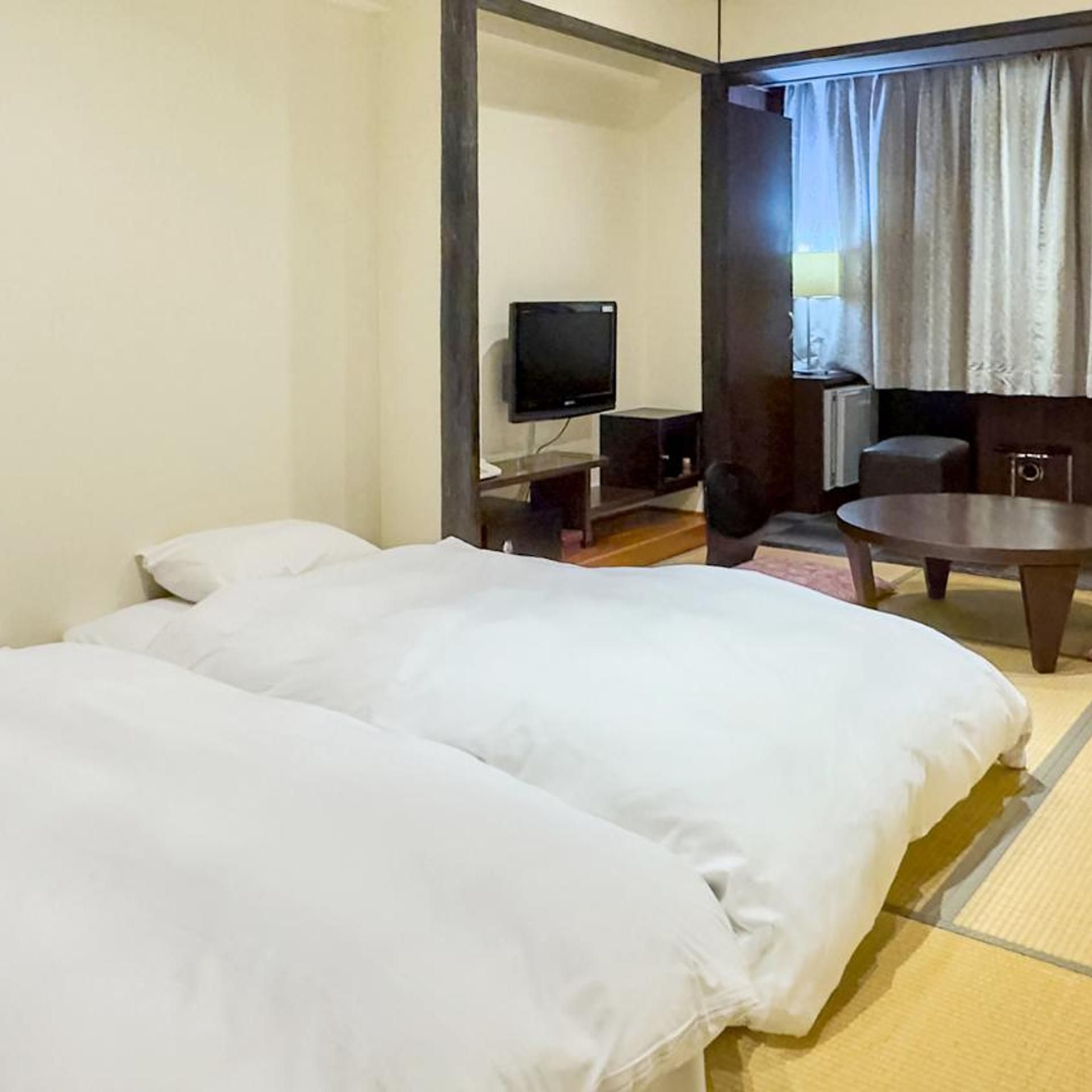 A hotel room with two beds, a television, a small table, and a view of the outdoors.