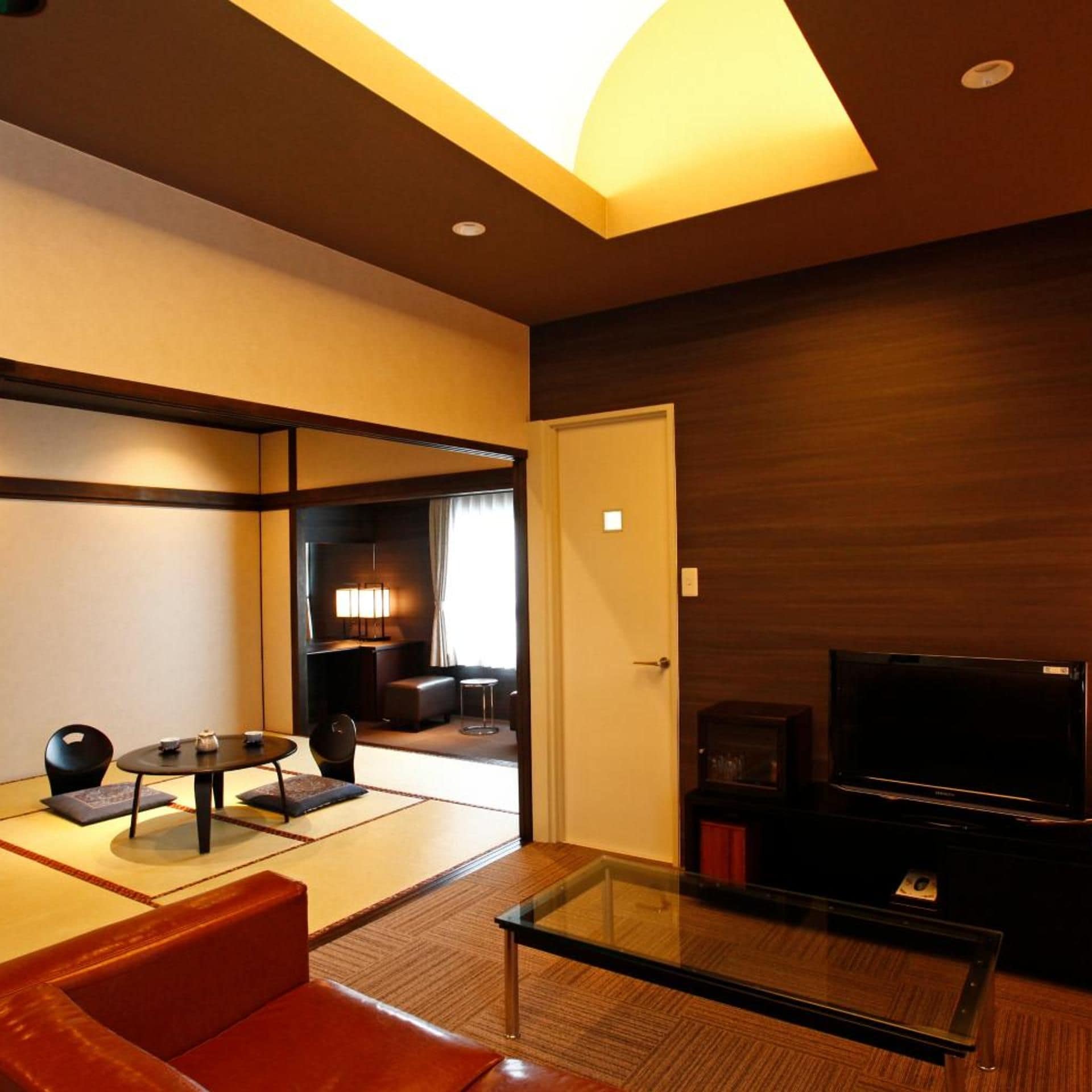 A modern living room with a glass coffee table, leather sofa, and a flat-screen TV.