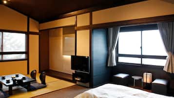 A hotel room with a bed, a TV, a small table, and a window with curtains.