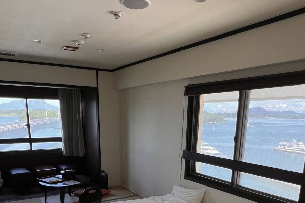 A hotel room with a bed, a desk, a chair, and a window with a view of the sea.