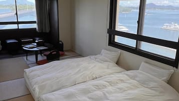A hotel room with a bed, a desk, a chair, and a view of the sea.