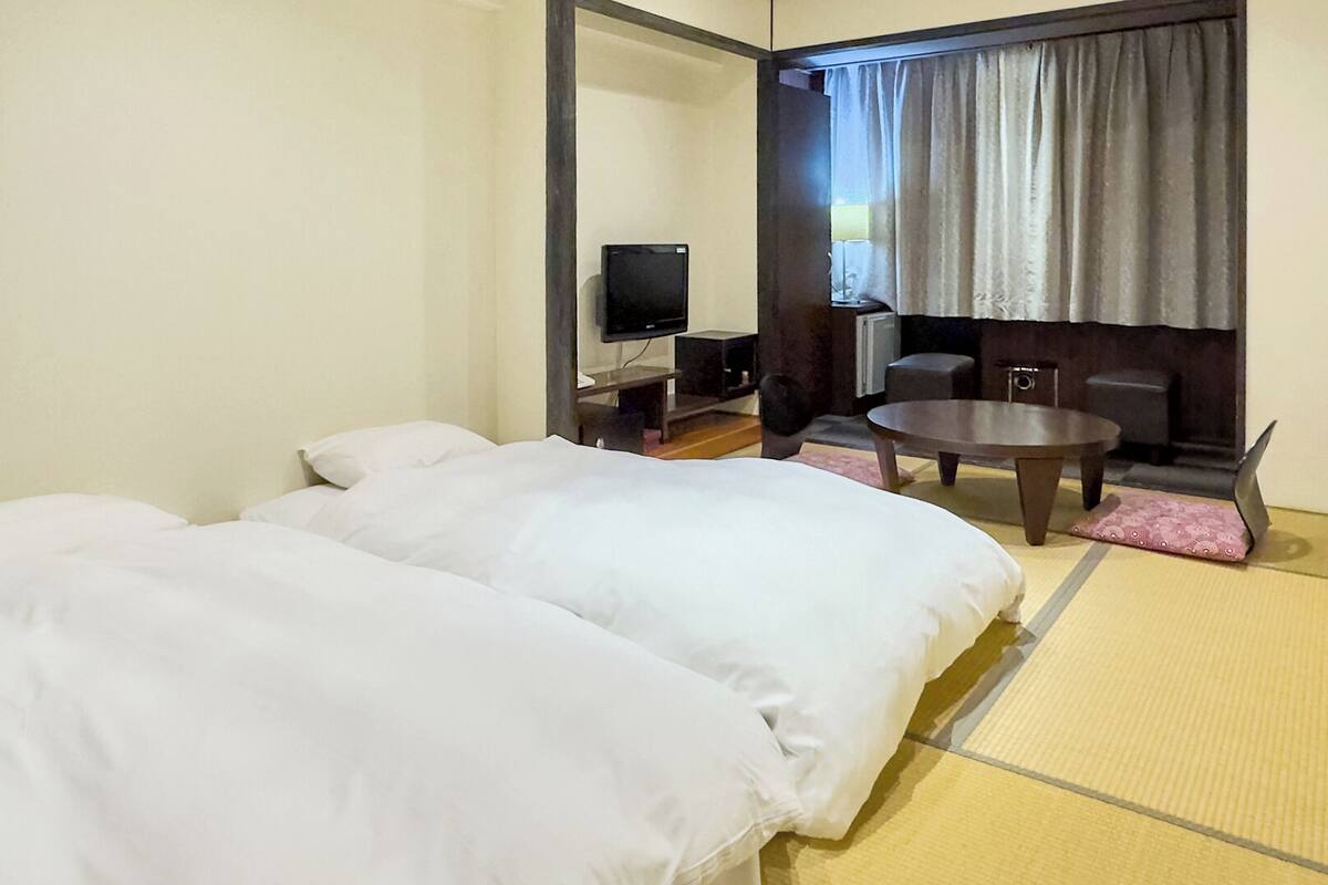 A hotel room with a bed, a desk, a chair, a television, and a window with curtains.