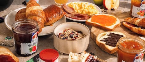 A breakfast table with croissants, ham, eggs, and various jams.