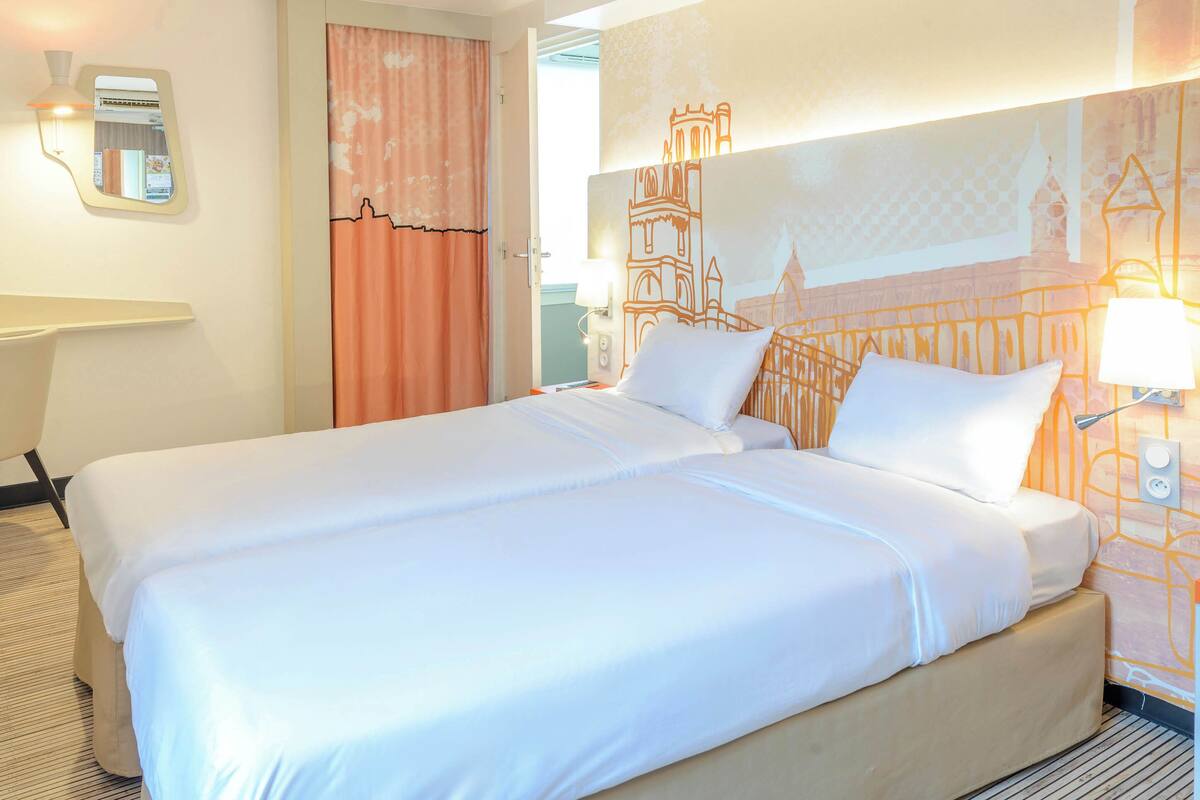 A hotel room with a large bed, a desk, and a mirror.
