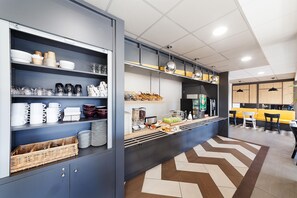 A modern kitchen with built-in shelves for dishes and utensils, a central island with a coffee machine, and a dining area with chairs and a yellow bench. - B&B Hôtel Albi (Albi)