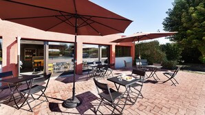 An outdoor patio with tables and chairs, large umbrellas, and a building entrance. - B&B Hôtel Albi (Albi)